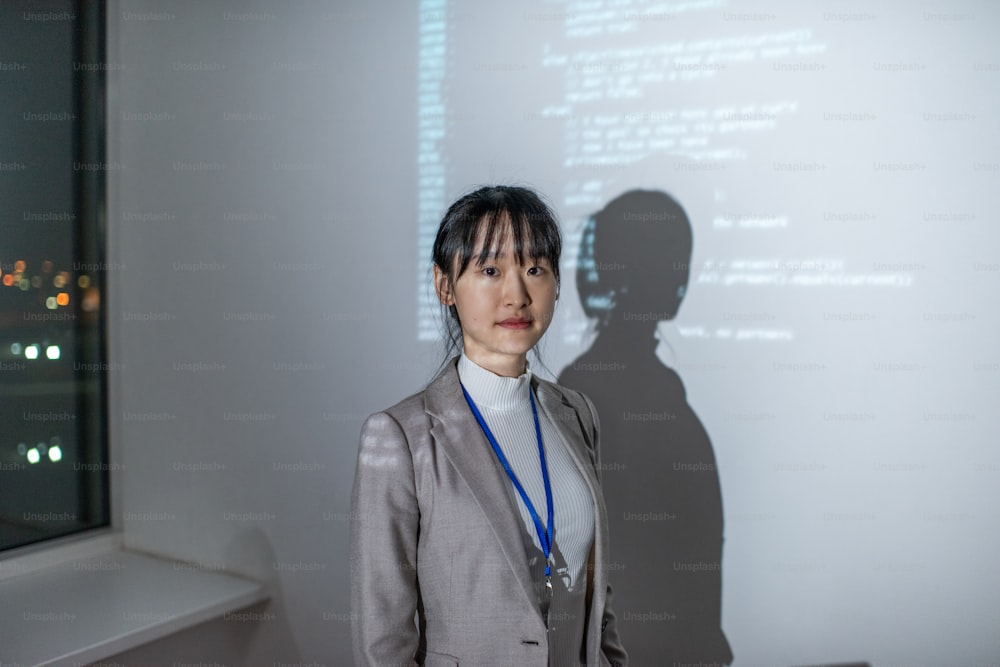 Jovem empresária asiática em formalwear em pé ao lado do quadro interativo com dados codificados durante a apresentação