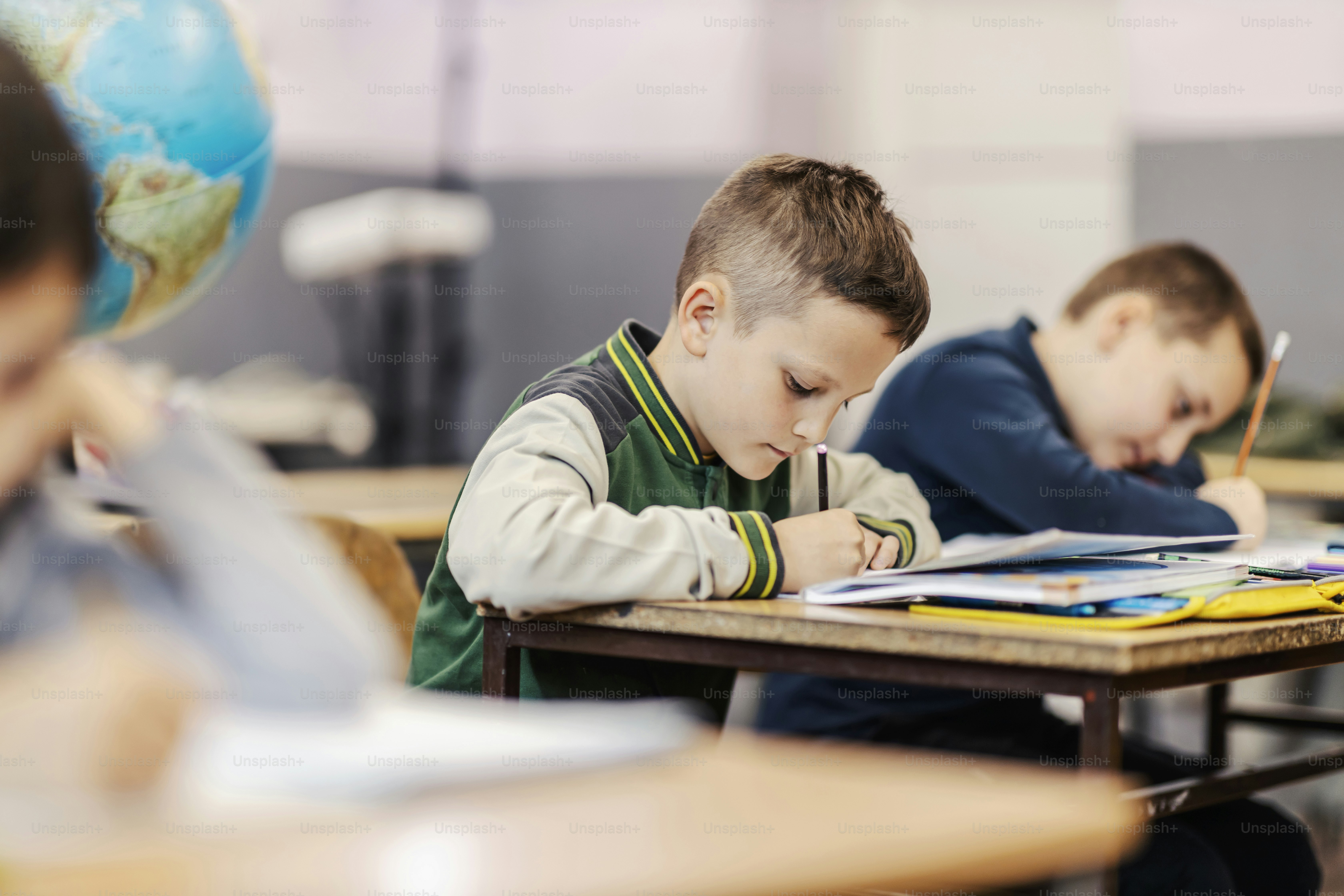 A pupil writes schoolwork while sitting at elementary school with classmates.