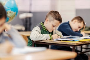Un alunno scrive i compiti mentre è seduto alla scuola elementare con i compagni di classe.