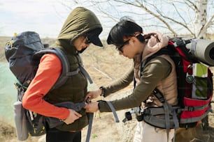 Vista lateral de una joven asiática que camina junto con su mejor amiga o hermana ayudándola a ajustar y arreglar la pesada mochila de viaje