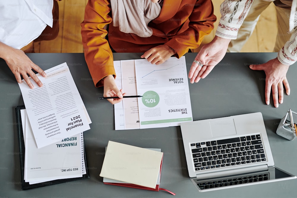 Above view of group of economists discussing financial documents with data at meeting while businessman explaining statistics