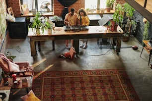 Young interracial couple in casualwear standing by long wooden table with dj booth and mixing sounds while creating new music