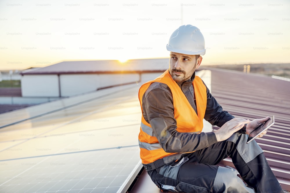 Un supervisore seduto sul tetto e con un pad di supporto per controllare i pannelli solari.