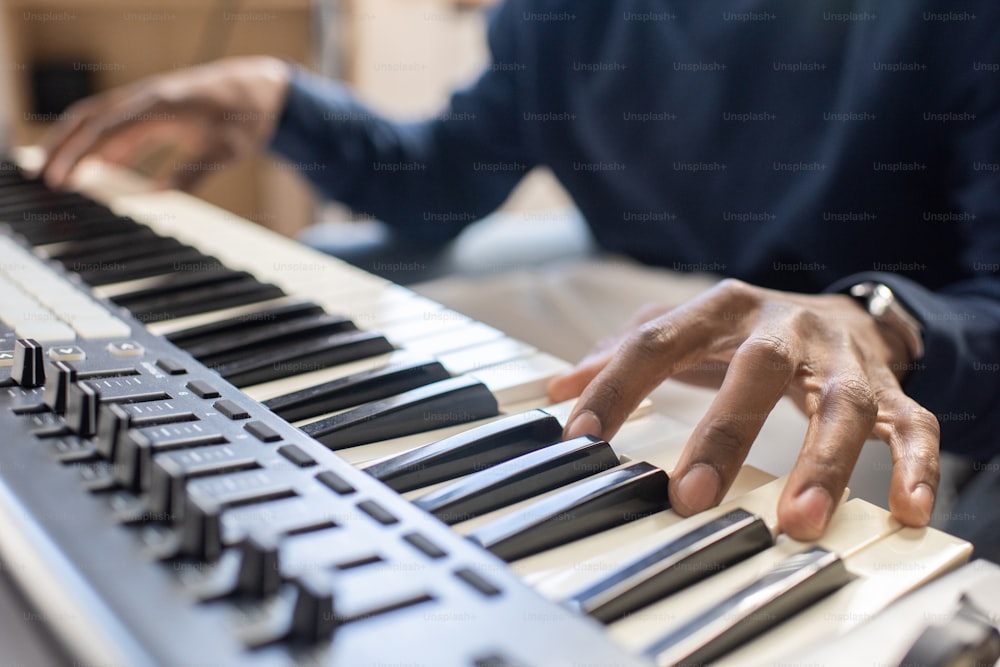 Dedos do jovem africano pressionando as teclas do teclado do piano enquanto ensina os alunos a tocá-lo