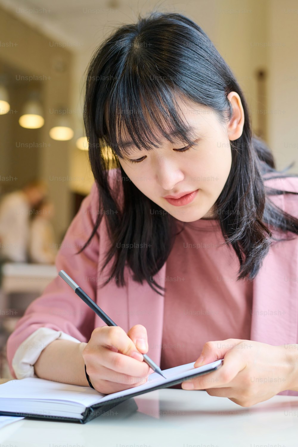 Asian businesswoman writing plans in her notebook while sitting at table in cafe