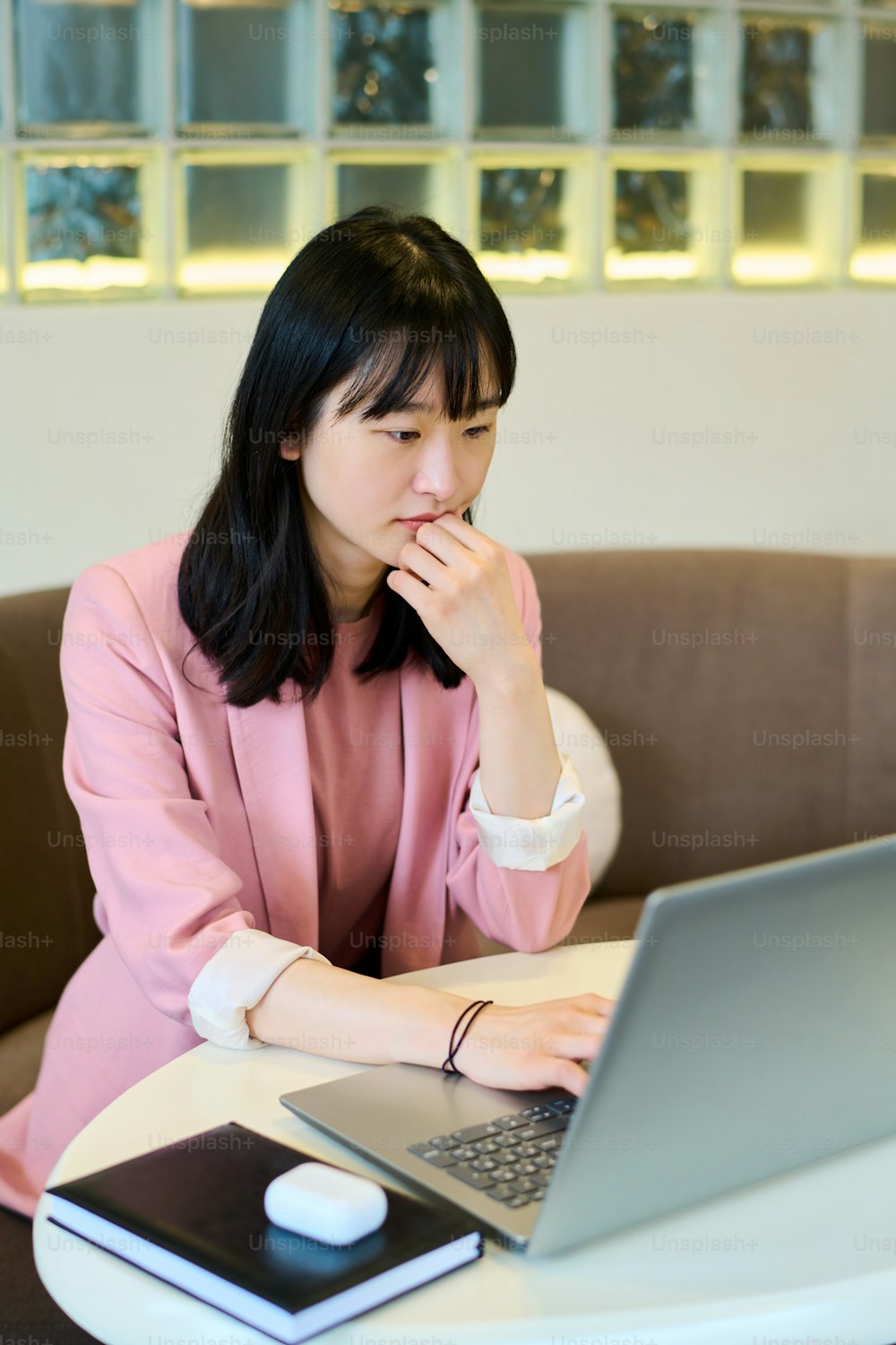 Joven trabajadora independiente sentada en la mesa en la cafetería mirando al monitor con expresión pensativa durante su trabajo en línea en la cafetería