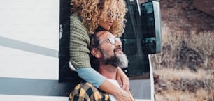 Travel with vehicle concept lifestyle with happy couple in love hugging at destination. Woman hug man with beard. Nature in background. Van camper vehicle transport for altarnative vacation