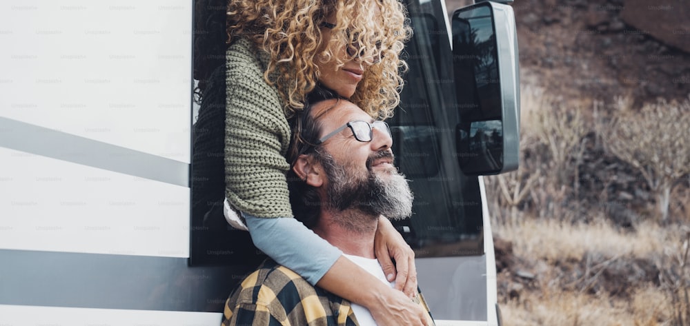 Travel with vehicle concept lifestyle with happy couple in love hugging at destination. Woman hug man with beard. Nature in background. Van camper vehicle transport for altarnative vacation