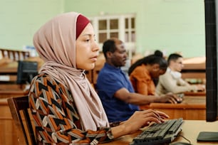 Mulher adulta jovem do Oriente Médio usando hijab trabalhando no computador na biblioteca da universidade