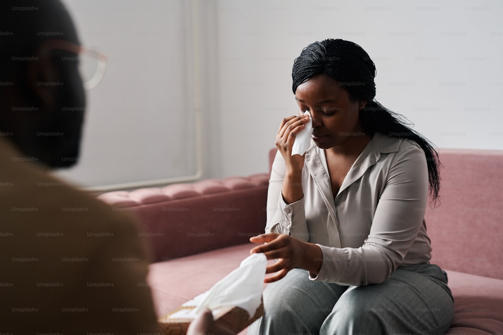 Jeune patiente stressée prenant un mouchoir en papier pour essuyer ses larmes tout en décrivant ses problèmes au psychanalyste lors de la séance