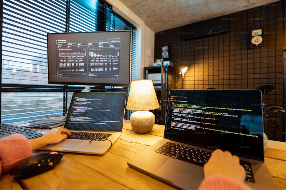 Female programmer writing programming code on laptops and desktop computer at cozy home workplace. Close-up on hands and keyboard