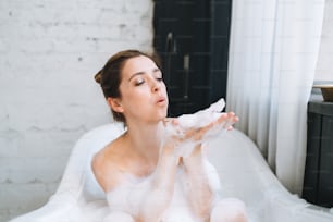 Jeune femme heureuse prenant un bain avec de la mousse à la maison, faites-vous plaisir
