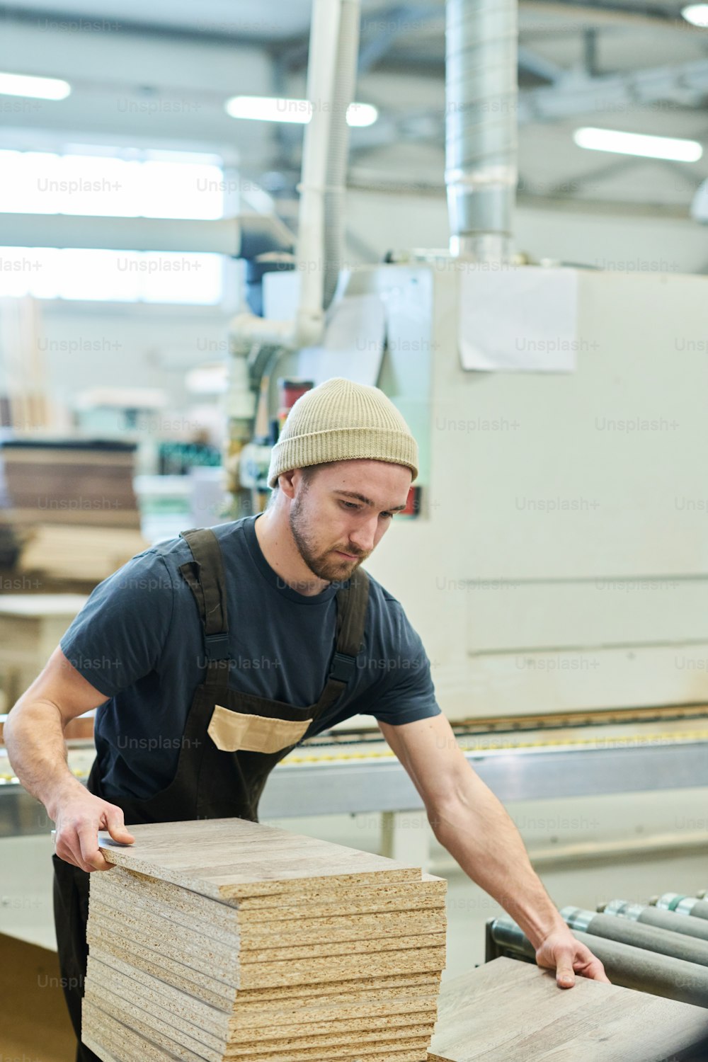 Jeune charpentier en uniforme travaillant avec des planches de bois à la machine dans une usine de meubles