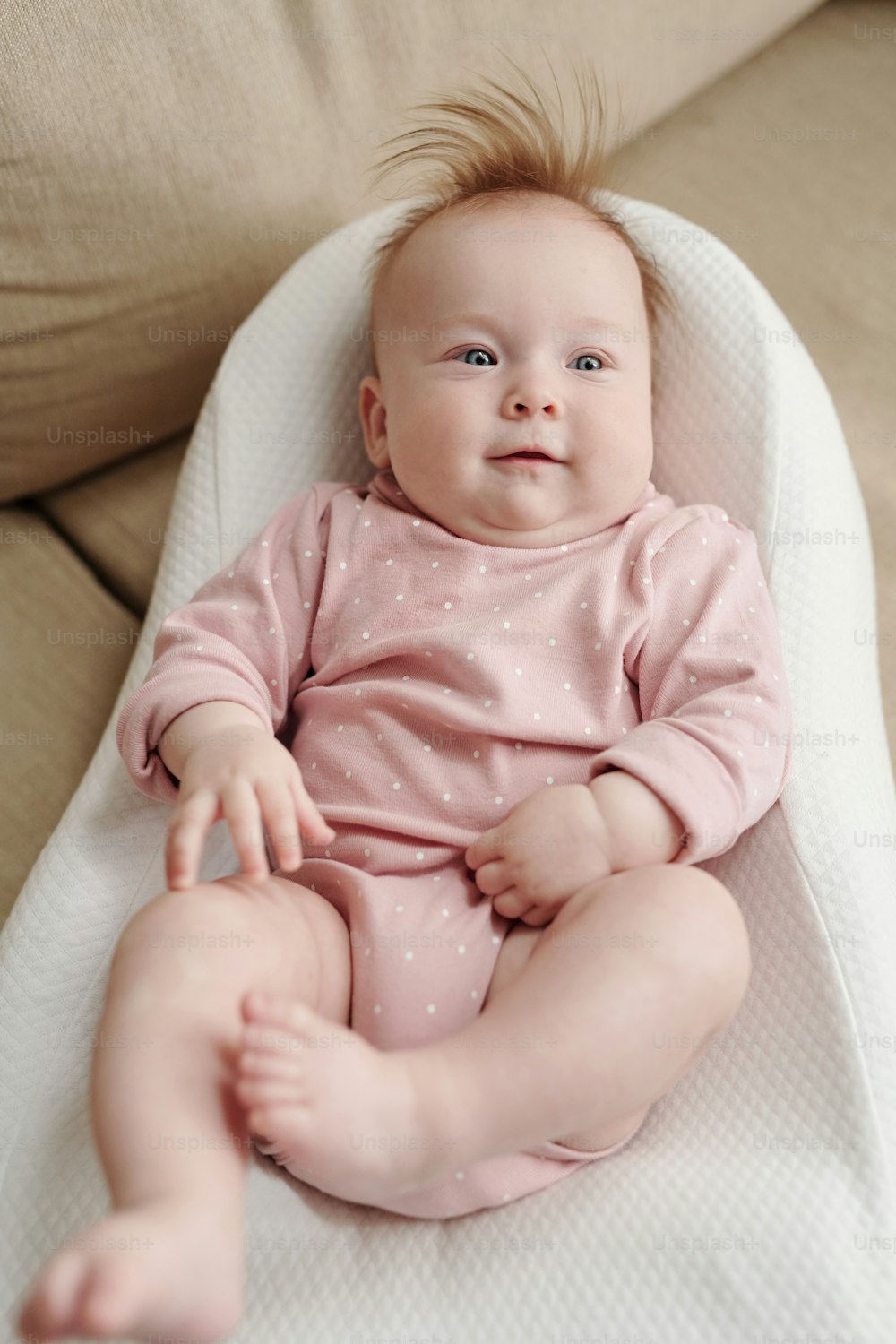 Adorable baby in pink clothes relaxing in small white soft bed in front of camera