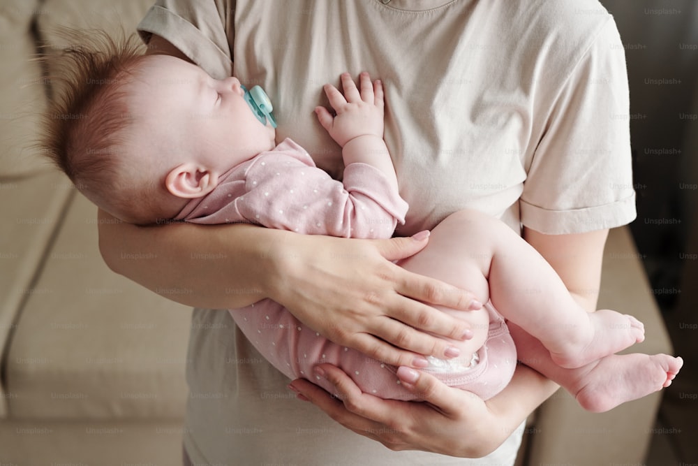 Cute tired baby girl with pacifier sleeping on hands of her careful mother