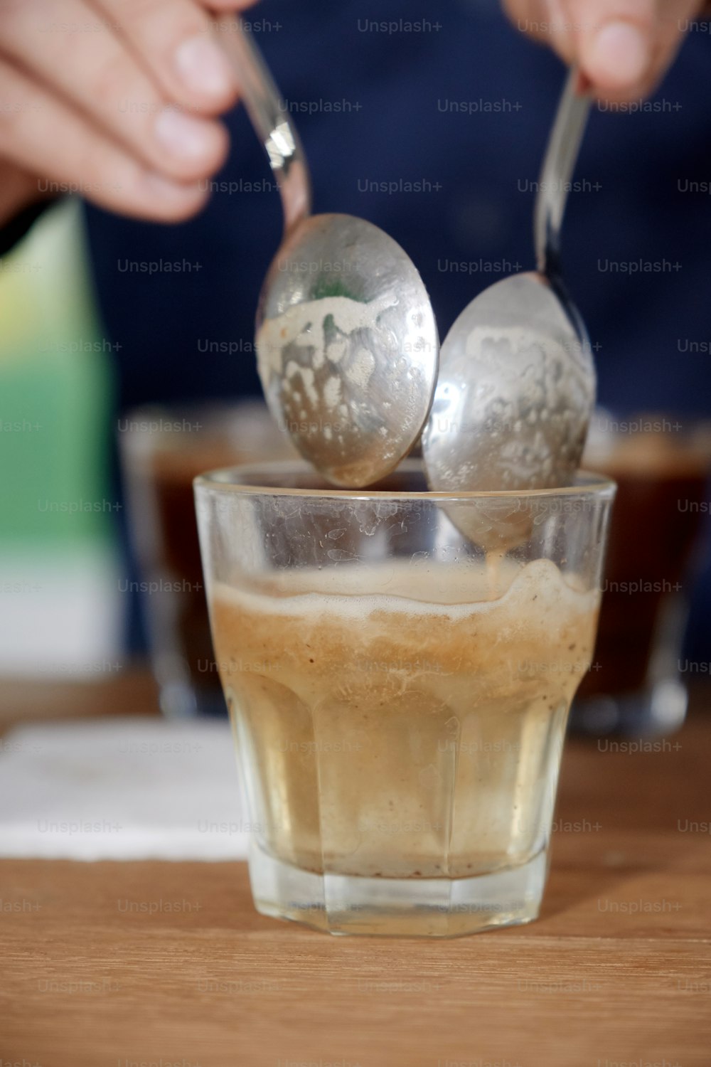 Nahaufnahme von Männerhänden, die frisch gebrühten Kaffee in einer Glastasse mit einem Löffel probieren, Kaffeegeschmack und -geschmack beim Kaffee-Cupping-Test für Barosta untersuchen