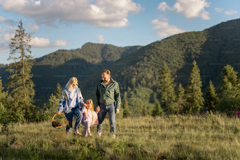 小さな女の子と若い白人のカップルは、山を旅しながら一緒に歩きます。自然の中で夏休みを過ごす幸せな家族