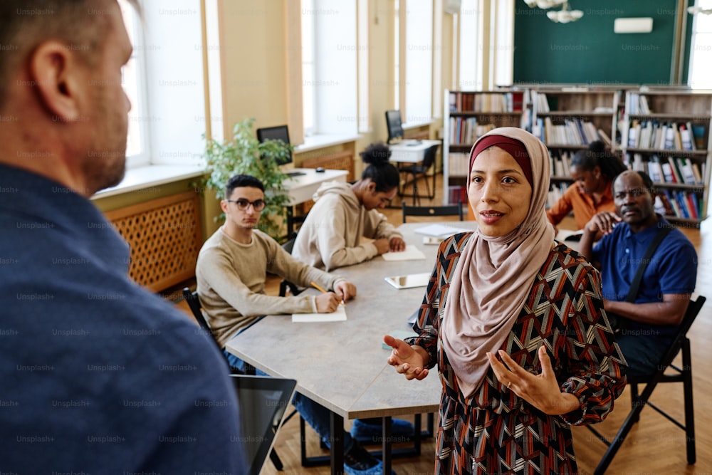 Mujer musulmana con hiyab de pie frente a un profesor de inglés que vuelve a contar la historia durante la lección para inmigrantes