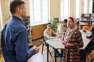 High angle shot of Muslim woman attending classes for immigrants standing in front of teacher trying to speak English