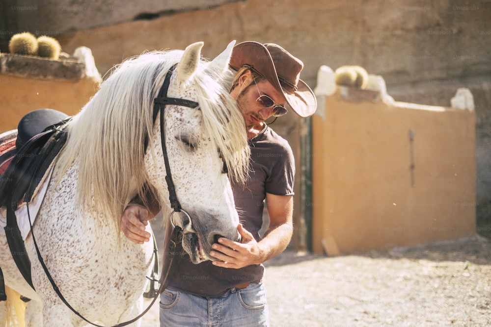 Ein schöner Mann wie Cowboy spricht mit seinem besten Freund Pferd, bevor er über die Berge reitet. Sonniger Tag und Hintergrundbeleuchtung. Leben Sie in der Natur und mit Tieren Konzept. Alternativer Lebensstil