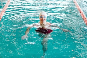 Active female swimmer in swimwear training in water at leisure in sports center