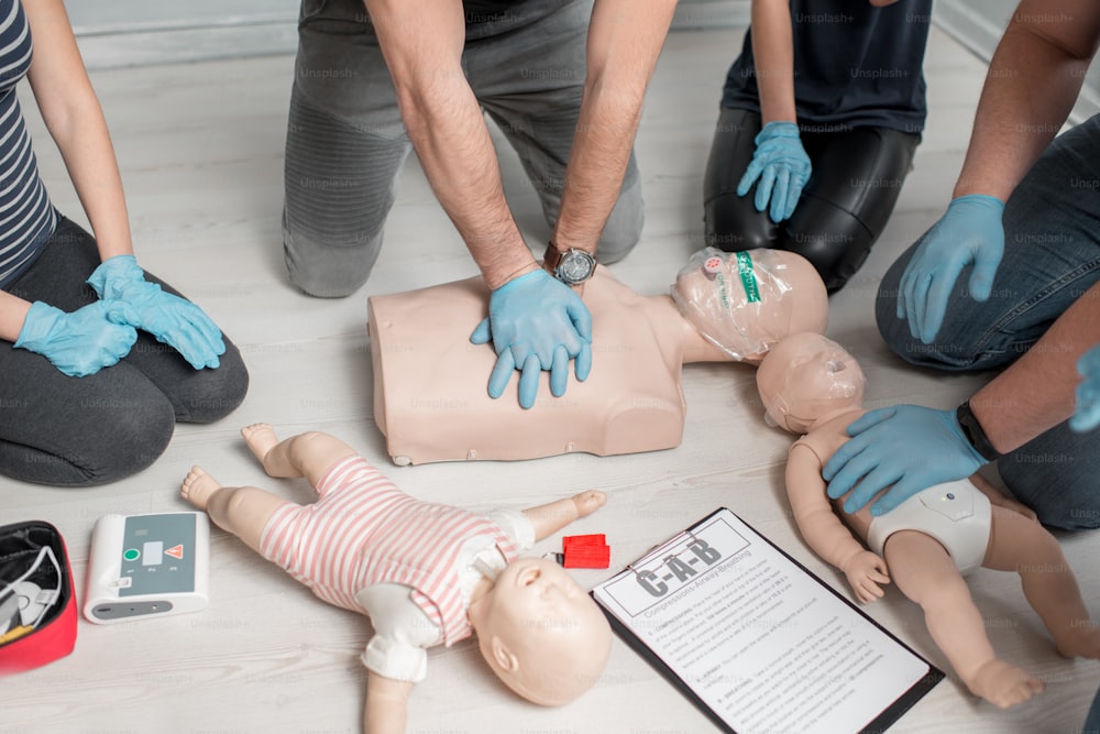 Groupe de personnes apprenant à faire des compressions cardiaques de premiers secours avec des mannequins pendant la formation à l’intérieur. Vue rapprochée sur les mains et les mannequins