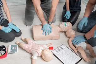 실내에서 훈련하는 동안 인형으로 응급 처치 심장 압박을 만드는 방법을 배우는 사람들의 그룹. 손과 인형의 클로즈업 보기