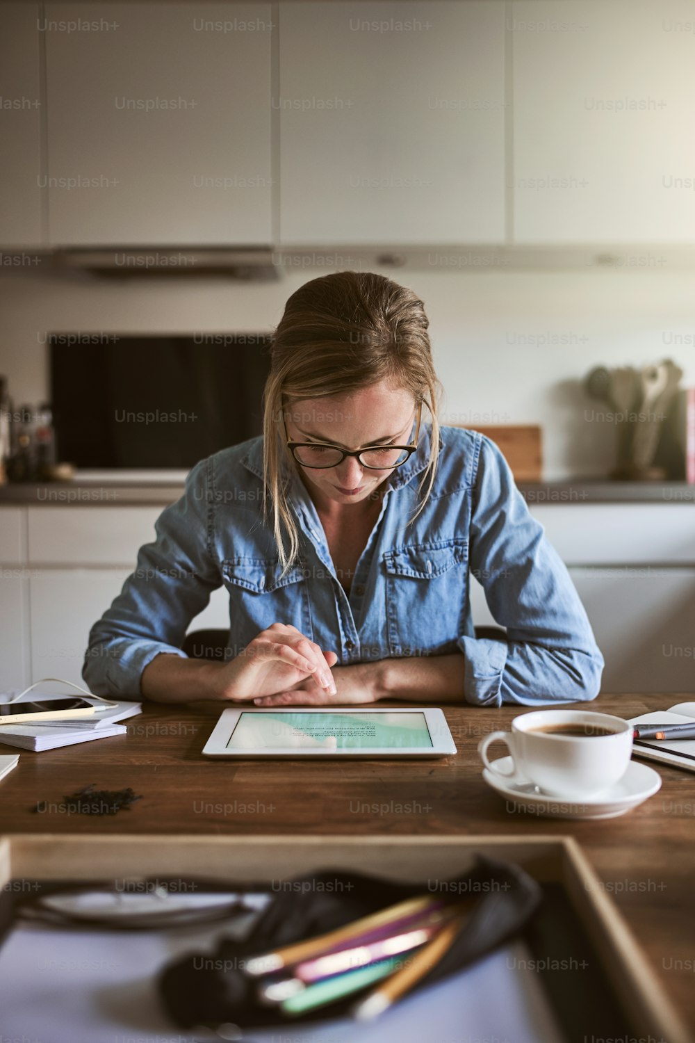 Giovane donna concentrata seduta al tavolo della sua cucina a casa che lavora alla sua piccola impresa con una tavoletta digitale