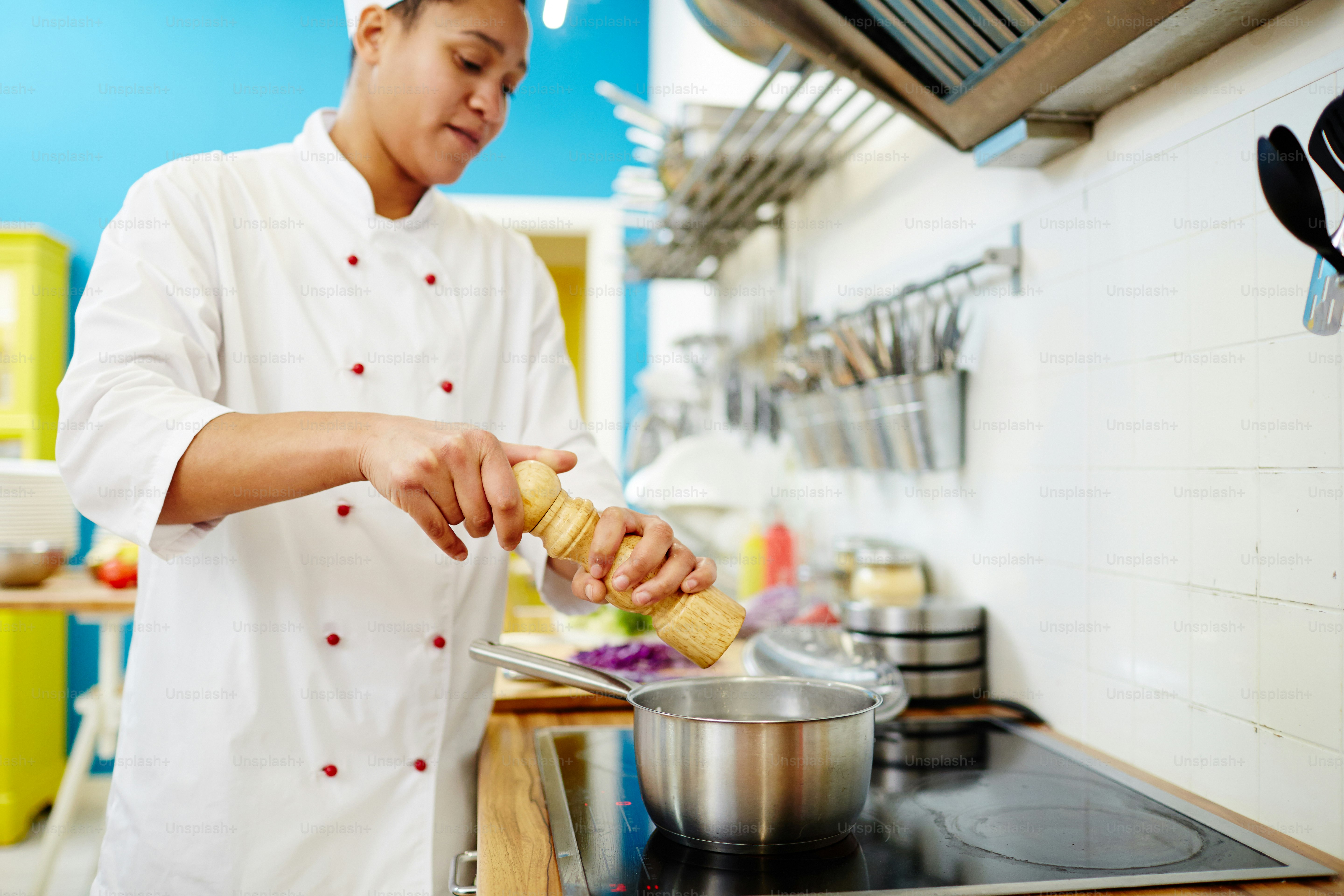 Chef adding salt or spices into stew cooking in pan on stove to enrich its taste