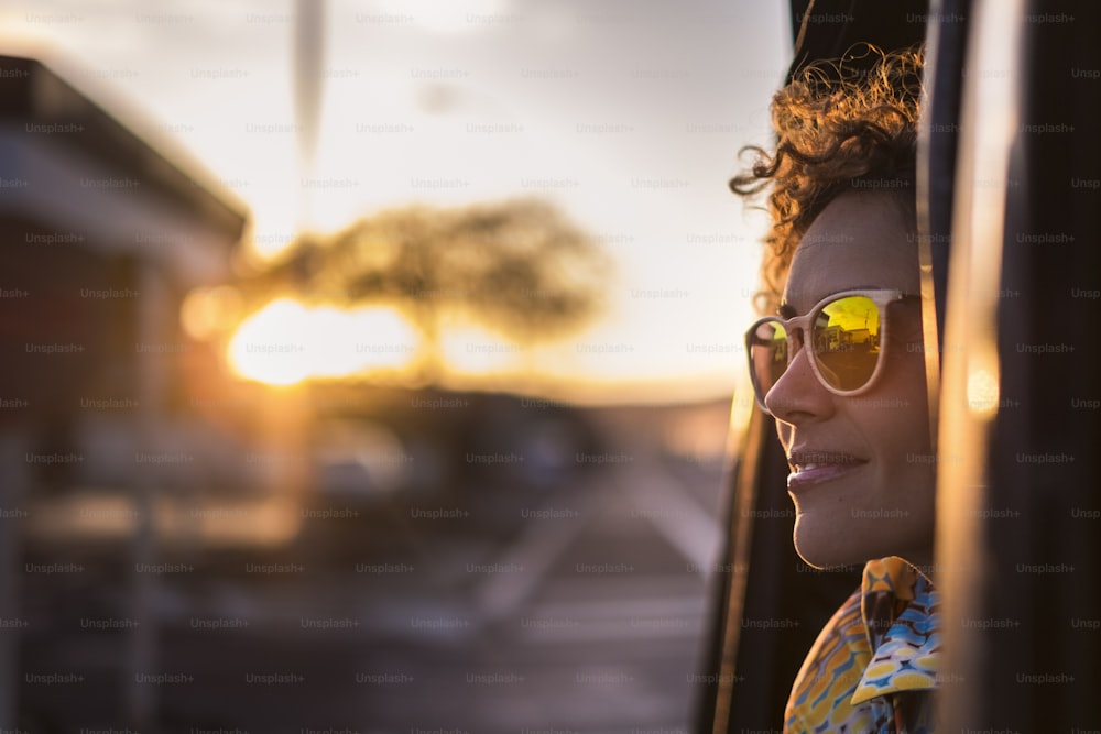 Hermosa mujer viaja en un automóvil mirando hacia afuera y disfruta de la luz de la puesta de sol dorada en su rostro. Buen estilo de vida y emociones tranquilas viajando por el mundo