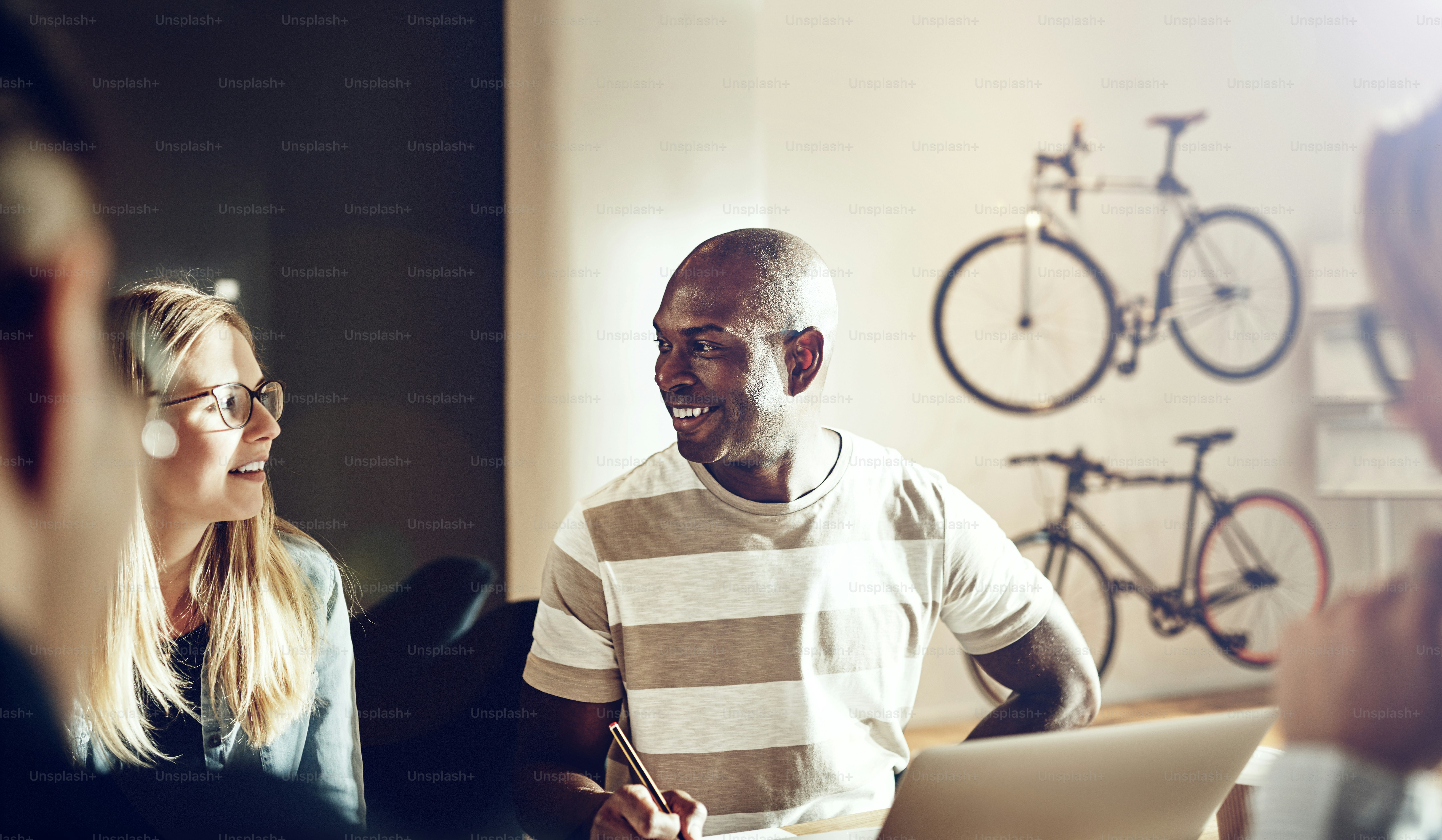Vielfältige Gruppe von Arbeitskollegen, die lächeln und ein Projekt diskutieren, während sie zusammen an einem Tisch in einem modernen Büro sitzen