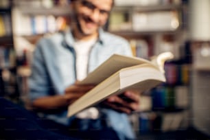 Close up book view while smiling young man reading in the high school library.