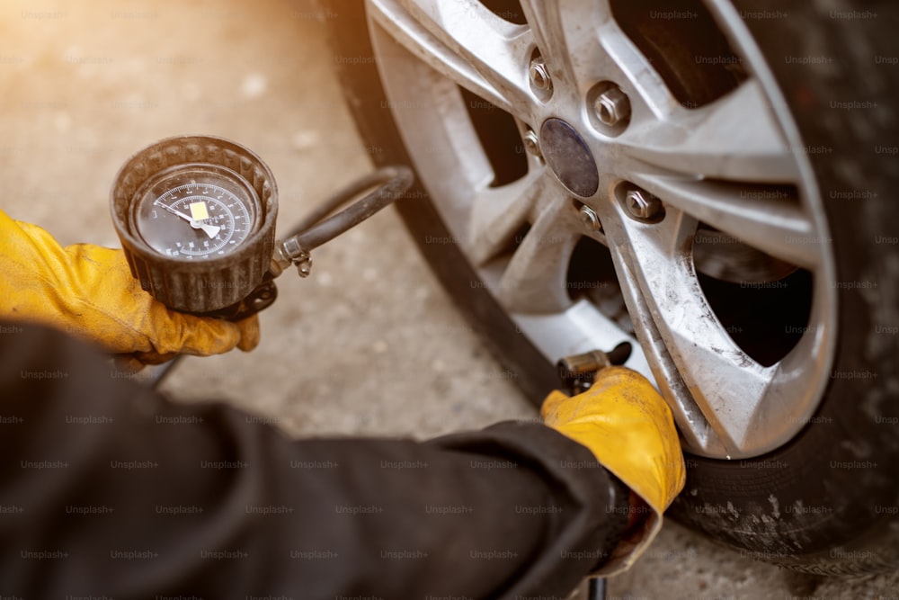 An experienced mechanic in orange gloves is placing air valve on a car wheel preparing to pressurize it.