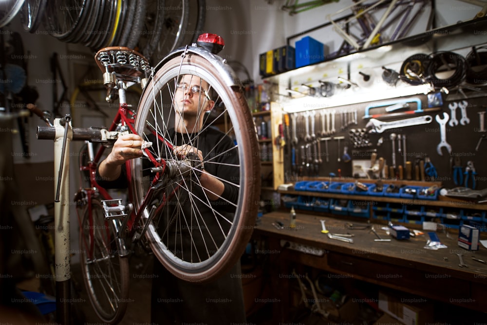 Jeune homme professionnel nettoyant le vélo dans l’atelier.
