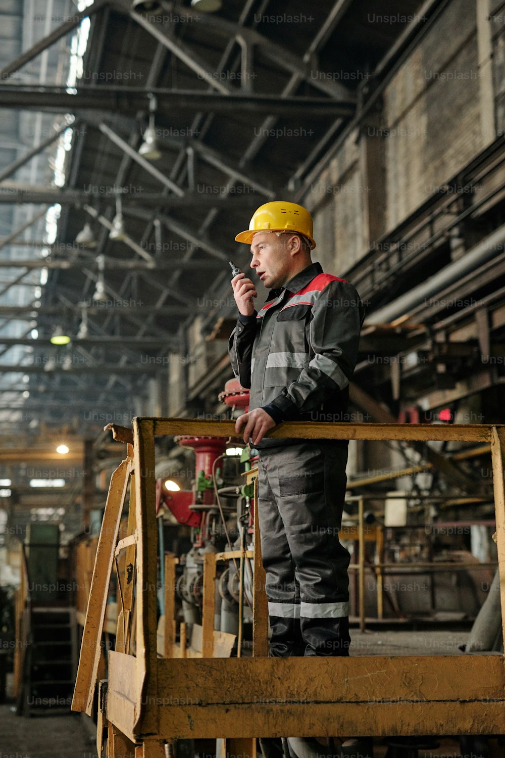 Foreman in workwear speaking in the radio set and controlling the work in the factory