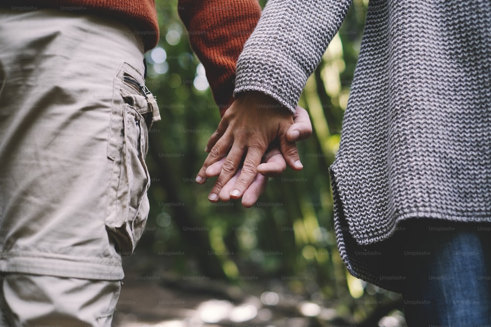 Close up of man and woman couple hands holding each other together with love and relationship and green woods nature forest in background - concept of friendship and healthy lifestyle