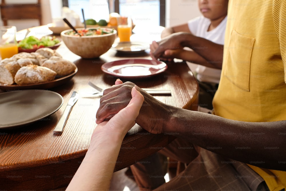 Hands of African man, his Caucasian wife and their son during pray by table before having dinner or breakfast