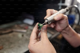 Gros plan d’une bijoutière méconnaissable façonnant une bague à l’aide d’un outil de polissage dans un atelier