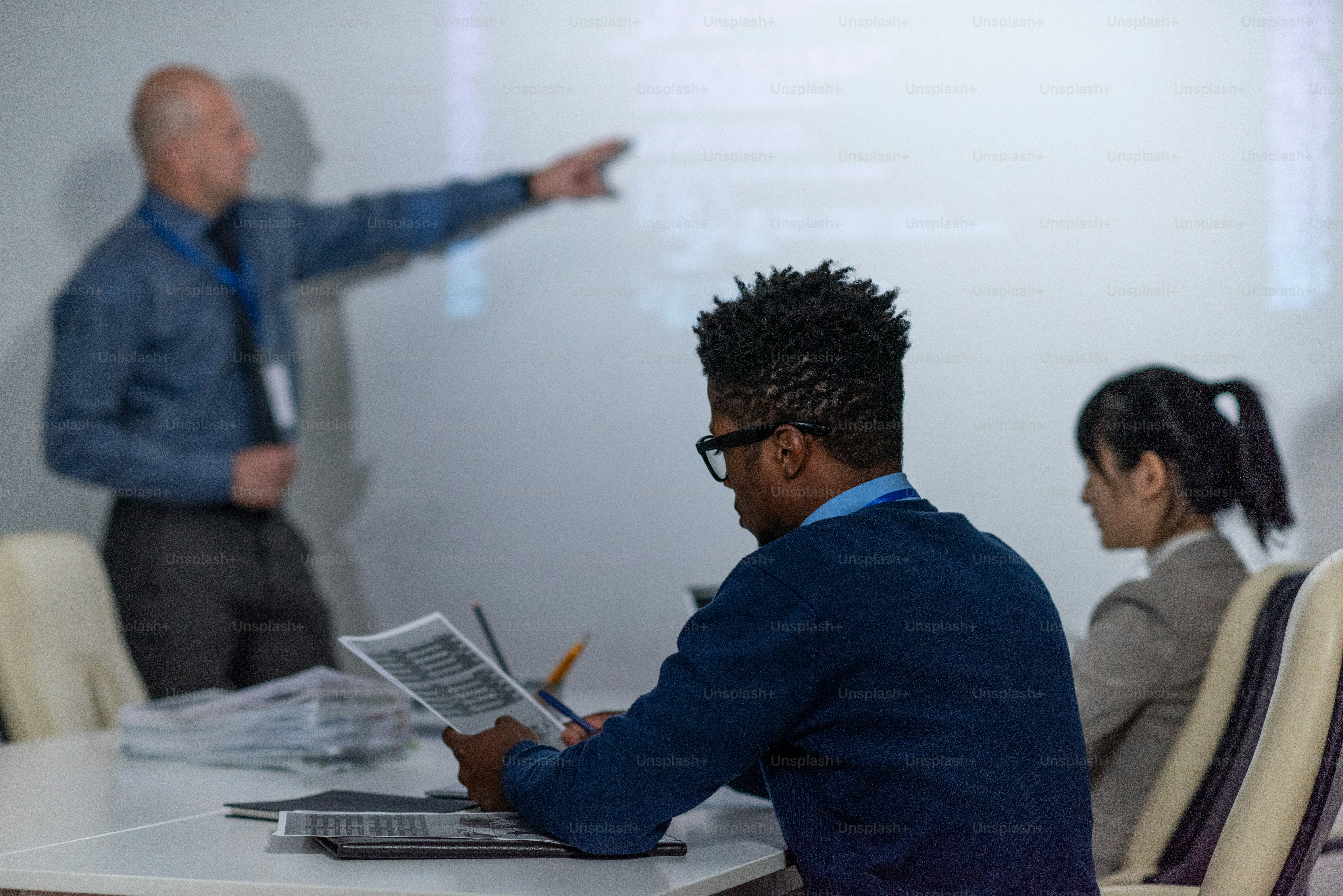 Young African programmer working with papers at seminar while mature businessman explaining data on interactive whiteboard