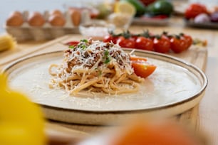 Assiette avec tas de pâtes italiennes avec de la viande hachée frite saupoudrée de fromage râpé au milieu de légumes frais et d’œufs