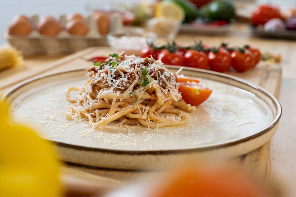 Plate with heap of italian pasta with fried minced meat sprinkled with grated cheese standing among fresh vegetables and eggs