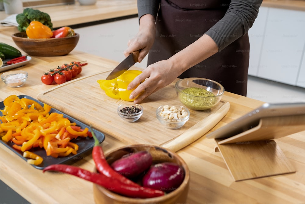 Young contemporary woman cooking vegetables while watching online recipe by table in the kitchen