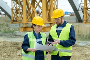 Two engineers working in team they standing on the site and discussing blueprint of future building