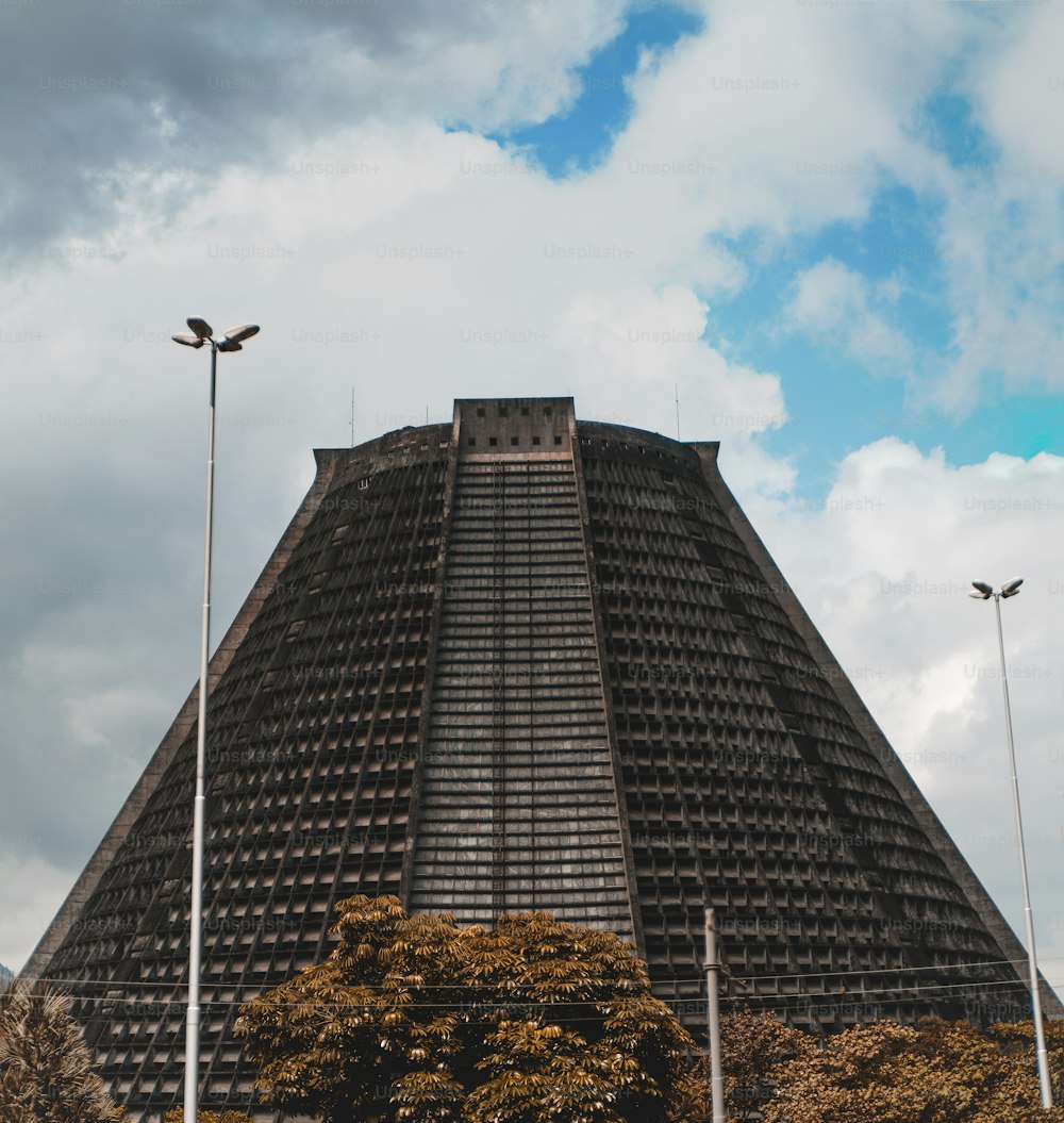 Close-up view of Metropolitan Cathedral of Rio De Janeiro (San Sebastian) made in modernism style; a cloudy bright summer day, with several lanterns, poles, and trees in the foreground
