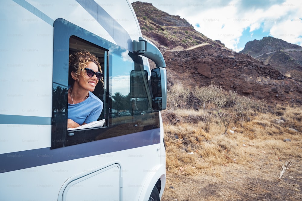 Happy adult woman smile and enjoy travel destination inside her camper van. Cheerful female people enjoy travel with camper van. Concept of van life and people renting motor home. Off grid parking