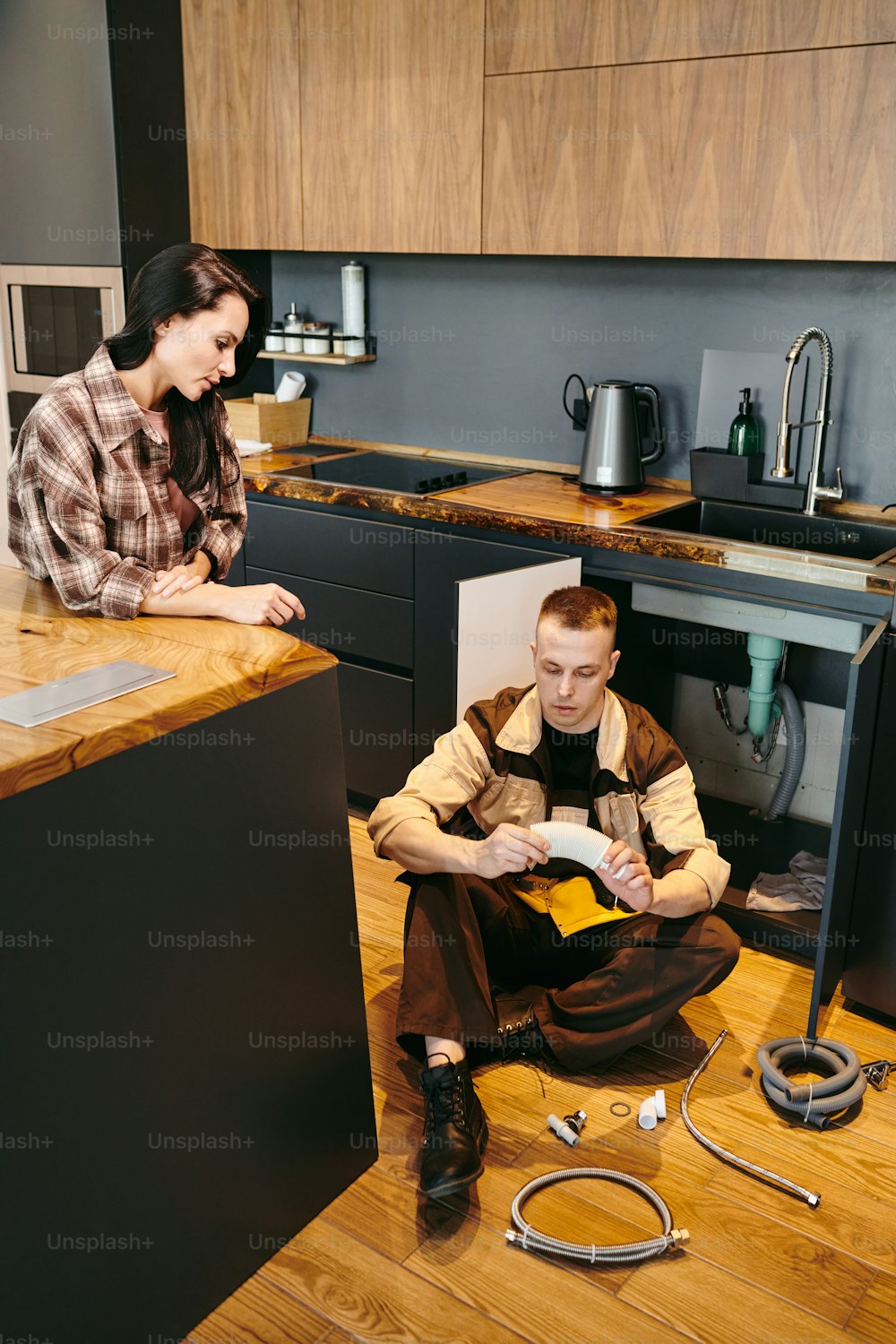 Young plumber and female client consulting about new pipe in the kitchen