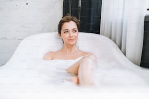 Jeune femme heureuse prenant un bain avec de la mousse à la maison, faites-vous plaisir