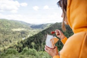 Young woman eats freeze-dried food for hiking from special packaging and enjoys great landscape while traveling high in the mountains. Concept of food and travel in nature