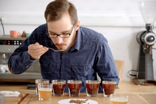 Retrato de un hombre que prueba el café recién hecho en una taza de vidrio, usando una cuchara, examinando el sabor y el sabor del café en la prueba de catación de café para barosta