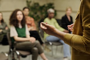 Hands of young business coach explaining information to group of employees at seminar while standing in front of audience